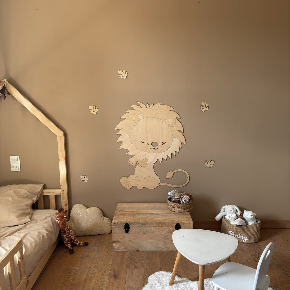 Léo le Lion XL en bois posé au mur d'une chambre d'enfant, entouré de feuilles